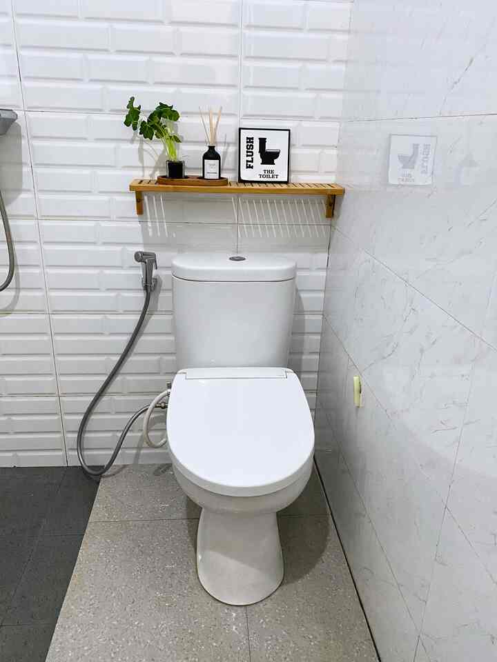 Compact bathroom with white tiled walls and bamboo shelf, featuring a clean, practical toilet at center