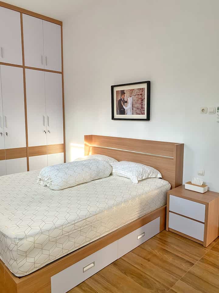 Bright white and wood tone bedroom featuring a wooden bed, wardrobe, and nightstand with clean and modern atmosphere