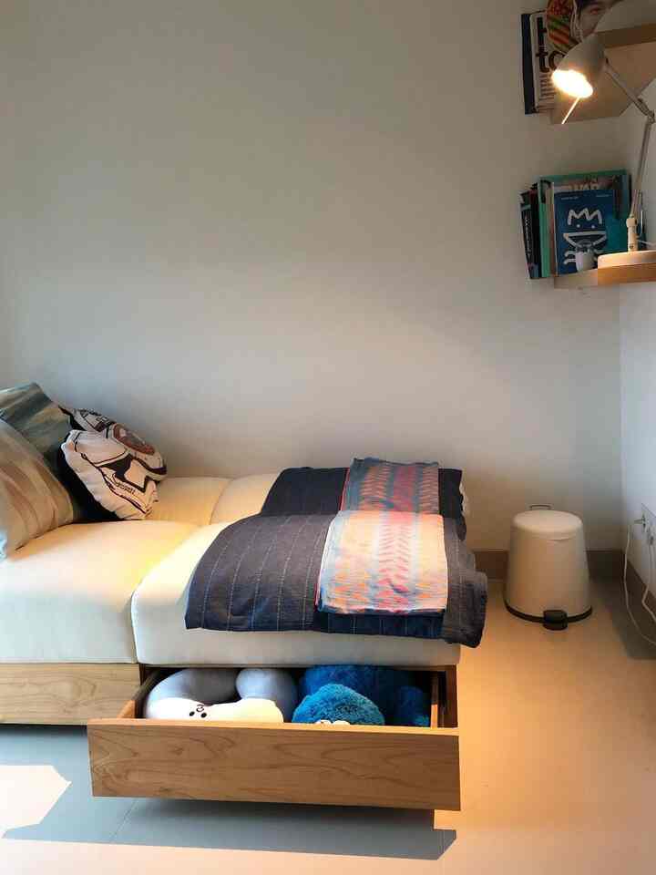 Modern bedroom with white and wood tones featuring a central sofa bed with an open storage drawer in a neat setting