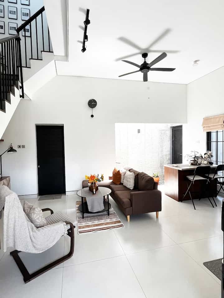 Modern living room and kitchen with white and black tones, featuring brown sofa and simple furniture creating a clean atmosphere