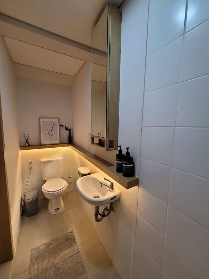 A narrow and simple powder room featuring white tiles and wood tones, with sink and toilet arranged for a cozy space