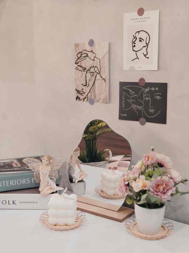 Soft beige and white tone desk featuring vase with flowers, candle, objet, and abstract art pieces on wall, creating a cozy K-style interior space
