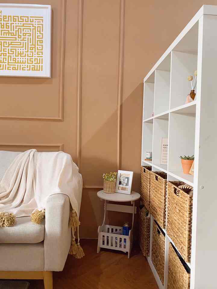 A natural modern living room with brown walls and wood-toned flooring. White sofa and organized storage shelves create a clean, cozy atmosphere.