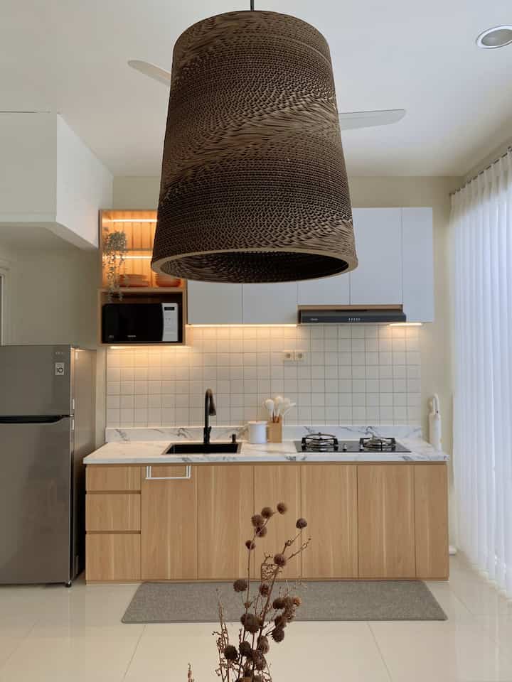 Modern natural kitchen featuring brown wood tone cabinetry and white tiled backsplash with warm lighting