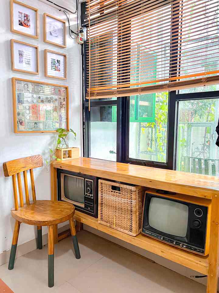 Wood tone corner storage space with vintage TVs, picture frames, and simple chair by window in a small room