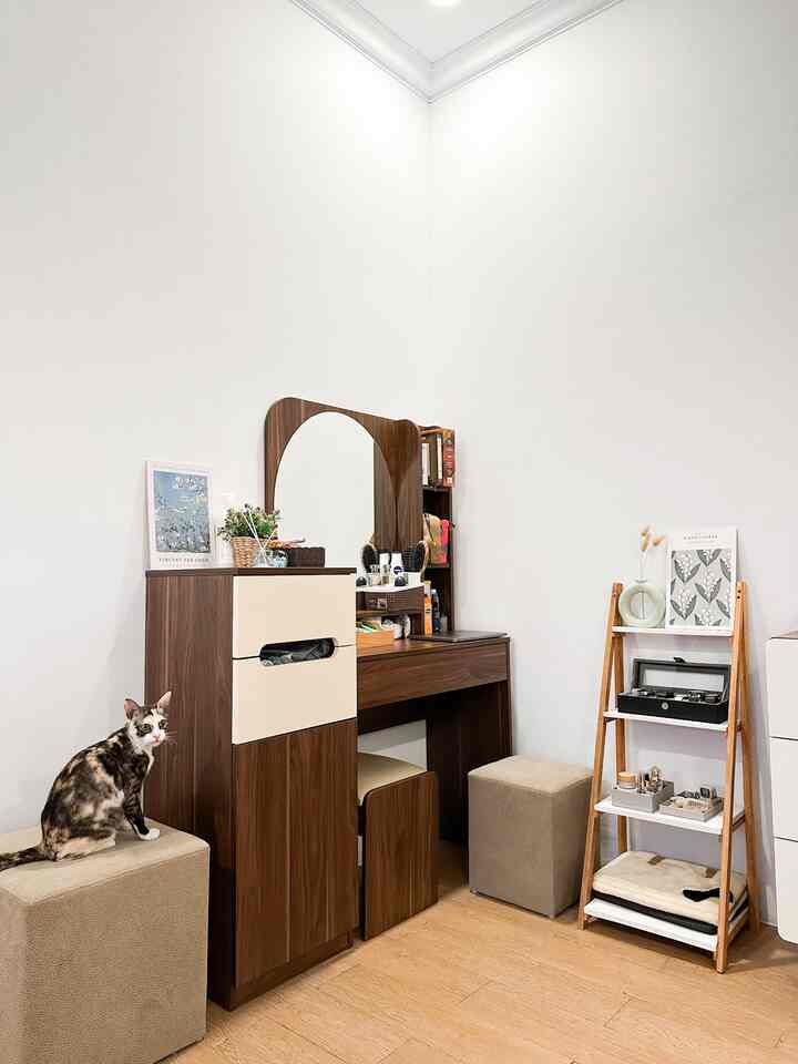 Natural wood tone bedroom featuring a vanity with mirror, dresser, mini shelves, and beige ottomans creating a cozy atmosphere