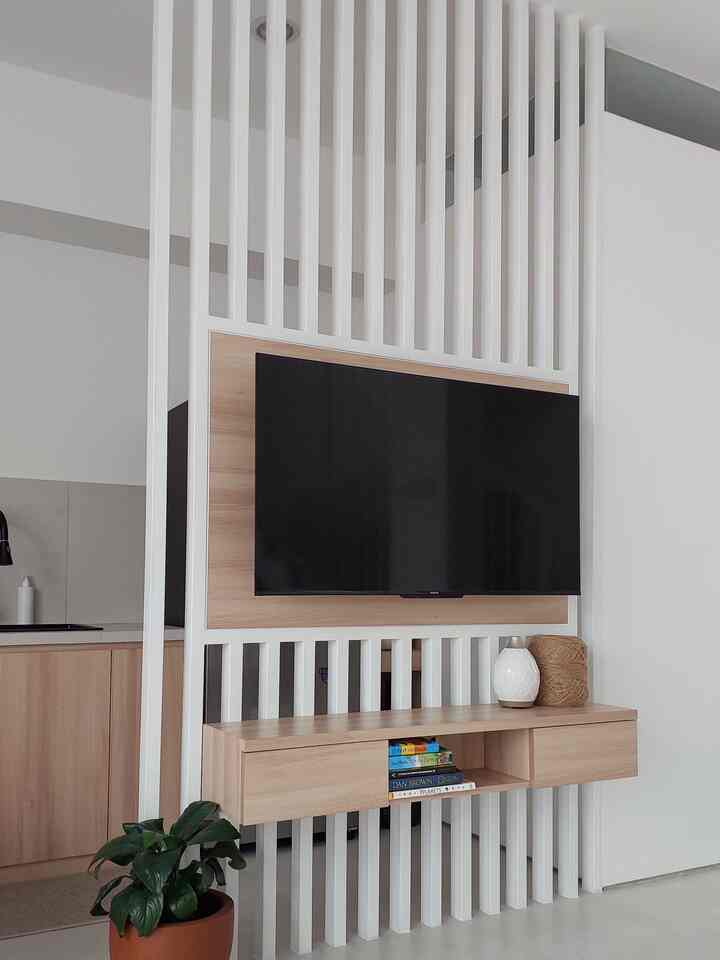 Minimal Scandinavian style living room and kitchen separated by a white and brown toned partition featuring a mounted TV space