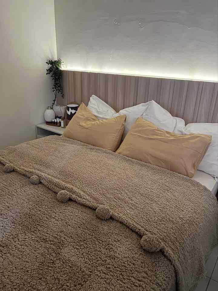 Beige and white toned Japandi style bedroom featuring a cozy bed with wooden headboard, table lamp and diffuser on the left side table