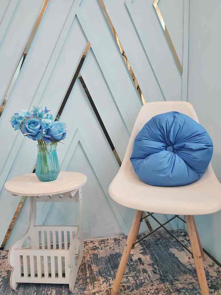 Pastel blue toned cozy corner featuring a white armchair with a blue cushion and gold-accented wall décor