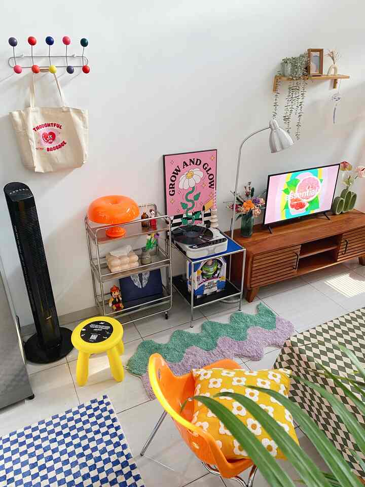 A vivid living room featuring an orange chair, yellow stool, pink poster, and artistic decor