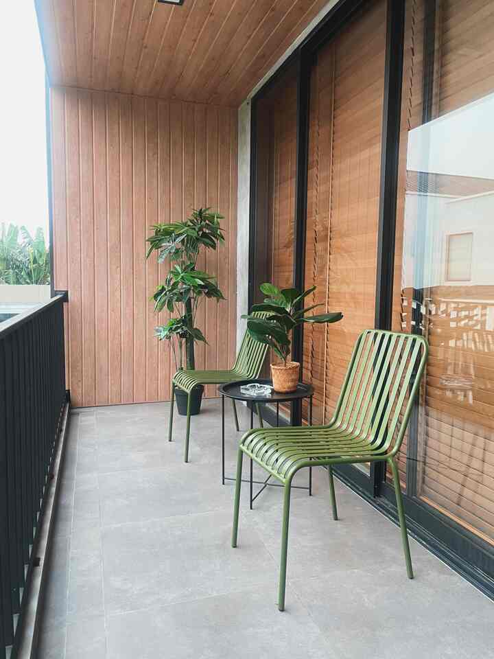 Balcony space with wood tone walls, two green chairs and potted plants