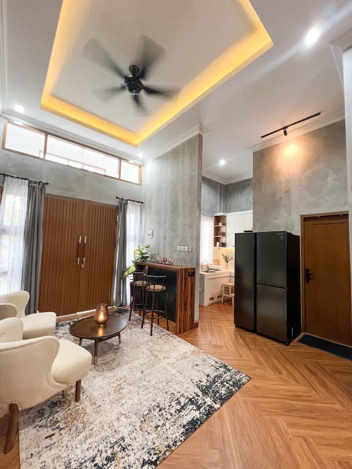 Light gray walls and wood-tone flooring blend in a natural living room with adjacent kitchen space