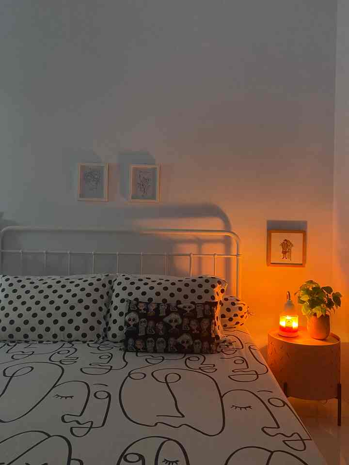Cozy white bedroom with warm orange lighting, patterned bedding, and framed art creating a homey atmosphere