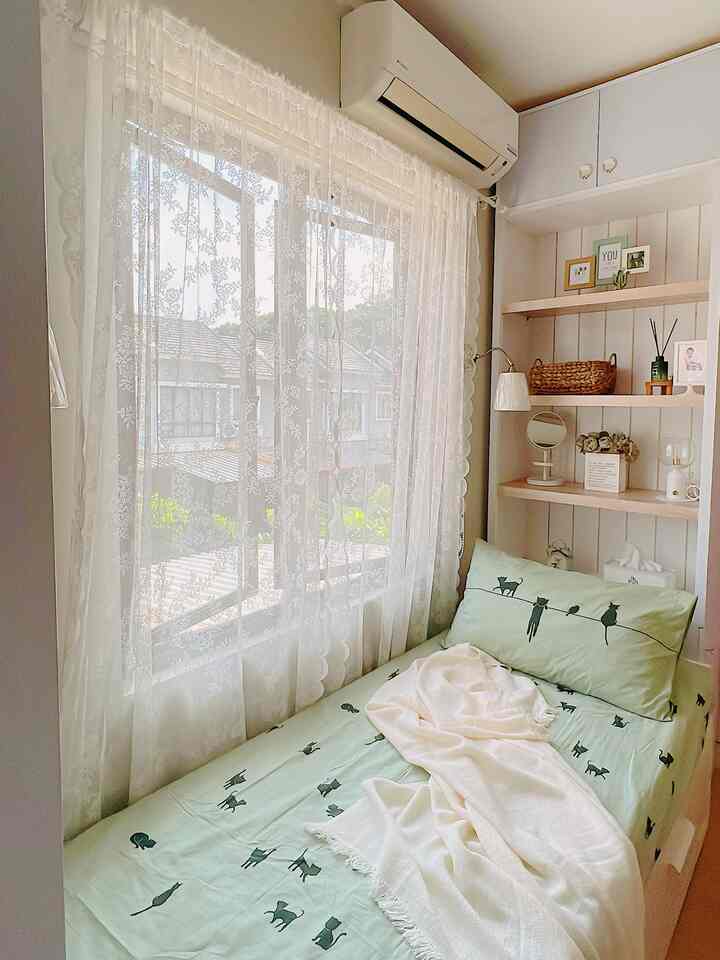 A cozy small kids' room with white and natural tones featuring curtains, wall shelves, and a kid's bed