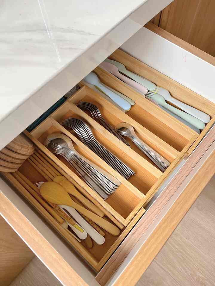 Neatly organized kitchen drawer featuring wooden storage tray with cutlery and utensils