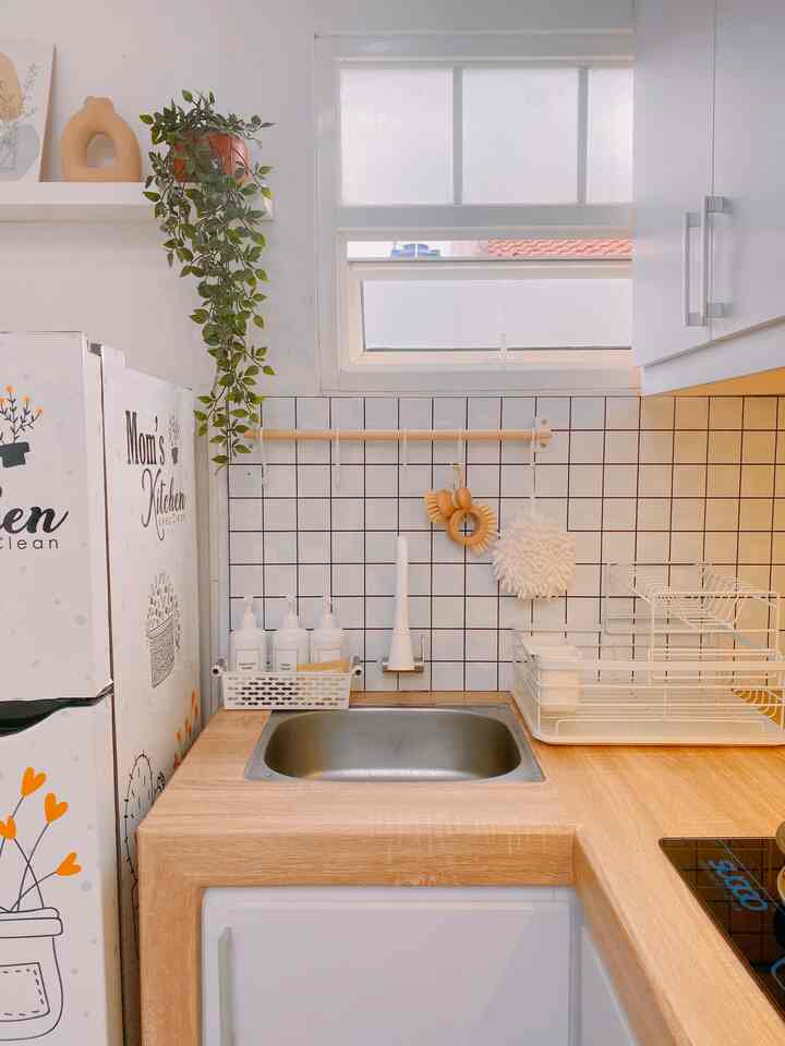 Modern kitchen space featuring white and wood tone sink area with neatly organized storage and hanging decor