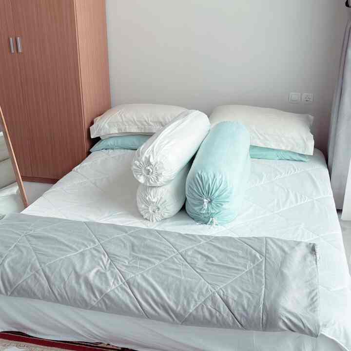 Natural color bedroom featuring a bed centered with a wooden wardrobe on the left, showcasing a clean and simple atmosphere