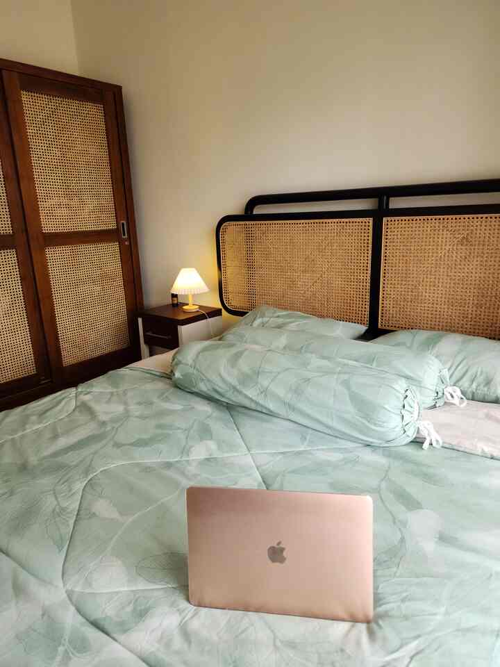 Natural tone bedroom featuring rattan headboard bed, wooden wardrobe, nightstand with table lamp, creating a cozy atmosphere
