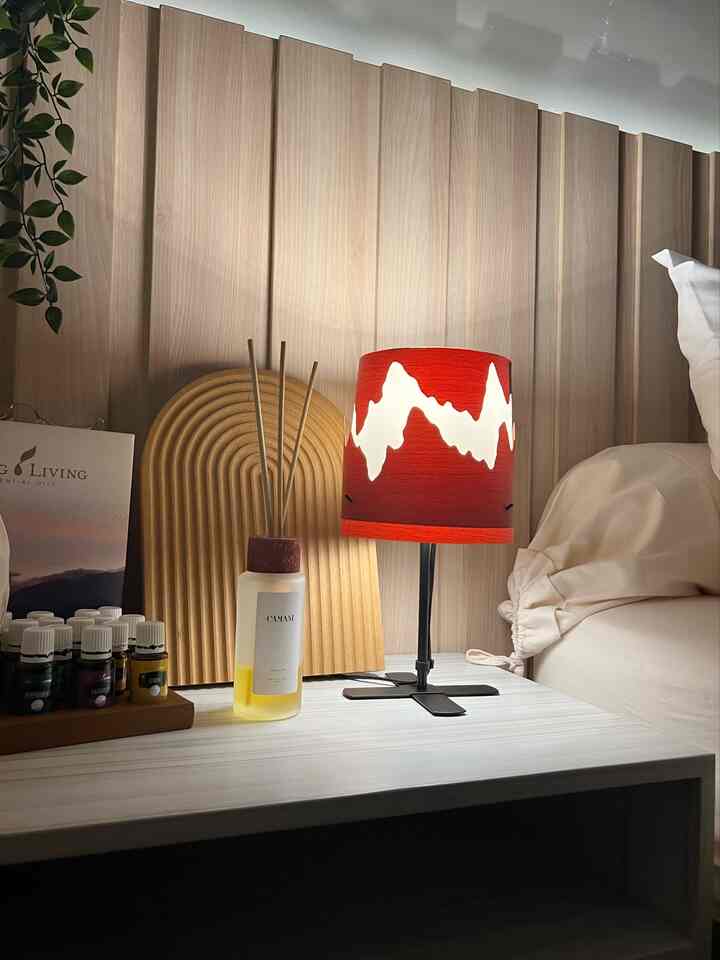 Natural wood tones and a red table lamp on a simple, cozy bedroom nightstand setup