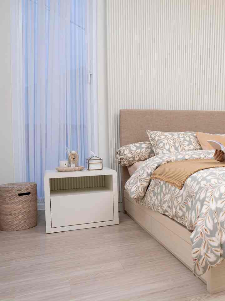 Beige and white toned bedroom featuring wood tone bed and nightstand, patterned bedding and curtains creating cozy atmosphere