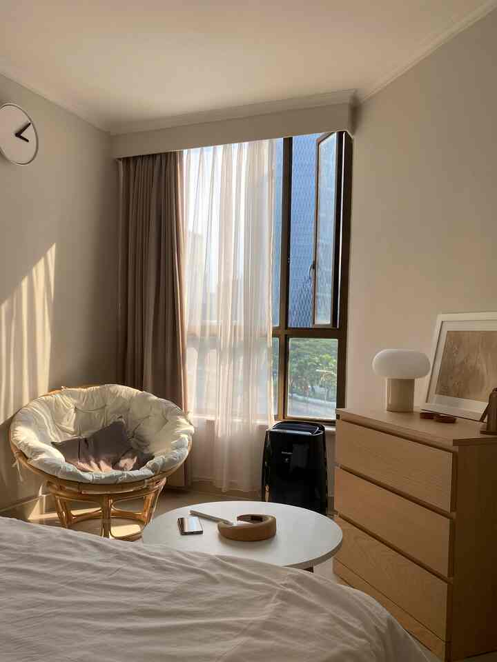 Beige natural-toned bedroom featuring white bed, rattan chair, and wooden dresser with cozy ambiance