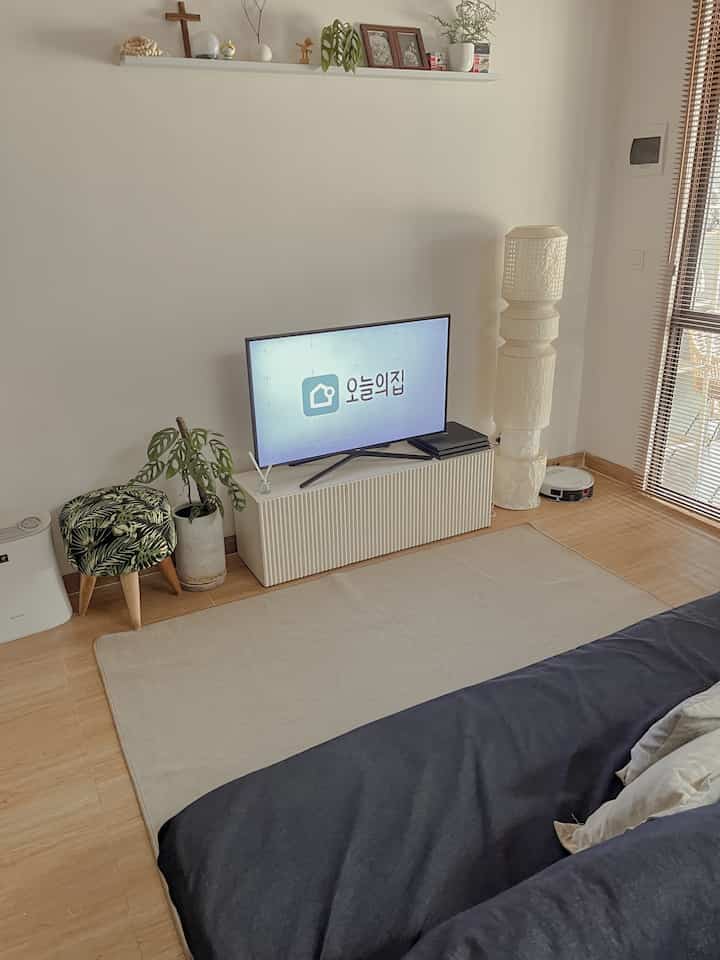 Ivory and wood tone living room featuring simple furniture, plants, and a cozy, natural atmosphere