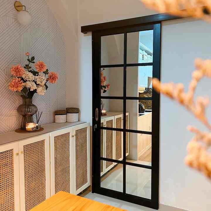 Modern storage area adjacent to kitchen in brown and white tones, featuring cane cabinets and black-framed mirror door