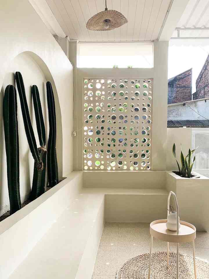 Natural beige-toned living area featuring circular perforated wall and tall cactus plants in a minimalist interior