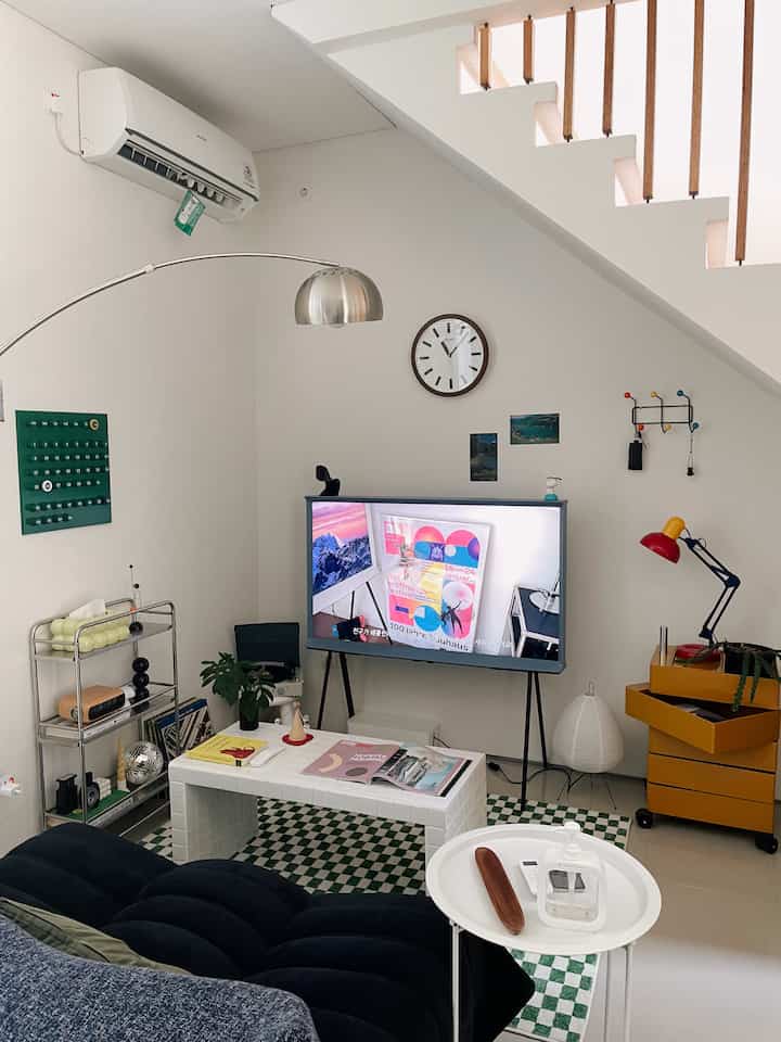 Monotone mid-century modern living room featuring centrally placed sofa and TV stand with small storage cart and shelves creating a cozy atmosphere