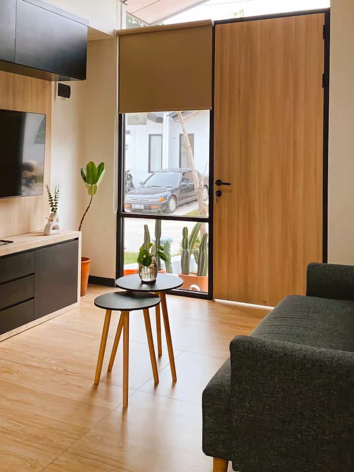 Natural color compact living room featuring a sofa, round coffee tables, TV stand, and various plants creating a cozy atmosphere