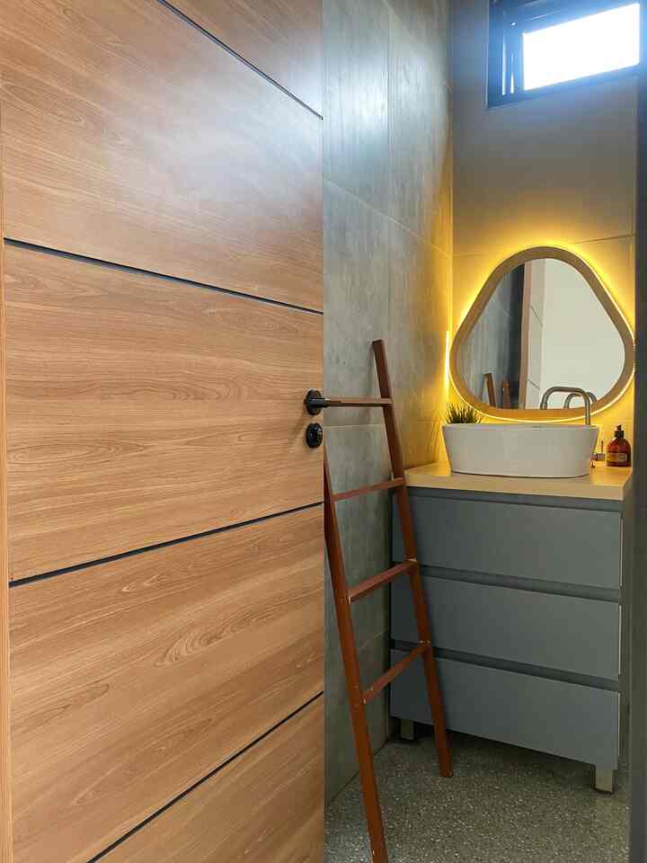 Natural wood tone door with industrial gray wall bathroom featuring triangular LED-lit mirror and sink vanity
