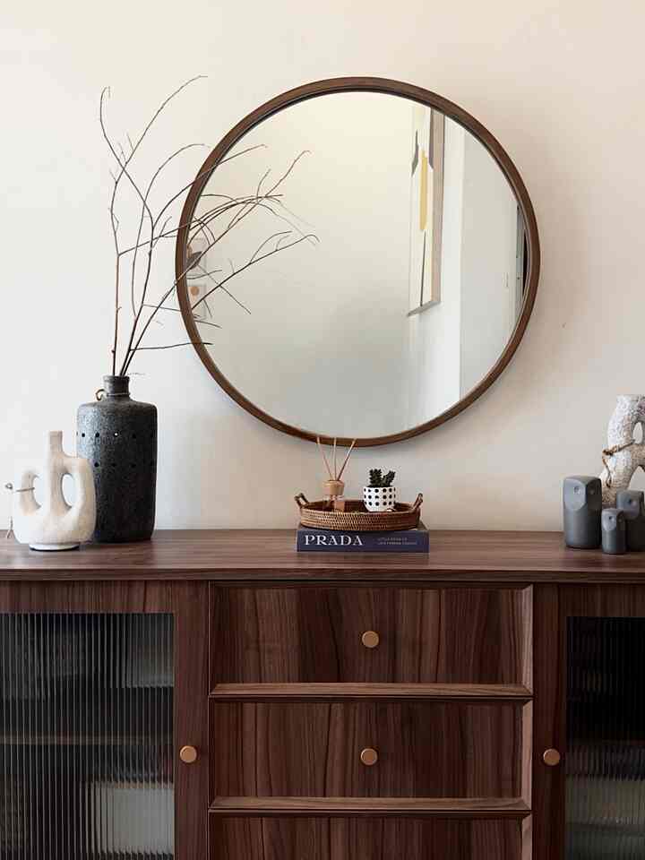 Entrance space with white walls and dark brown wood tone cabinet, featuring a round mirror and vintage-style vases for a natural atmosphere