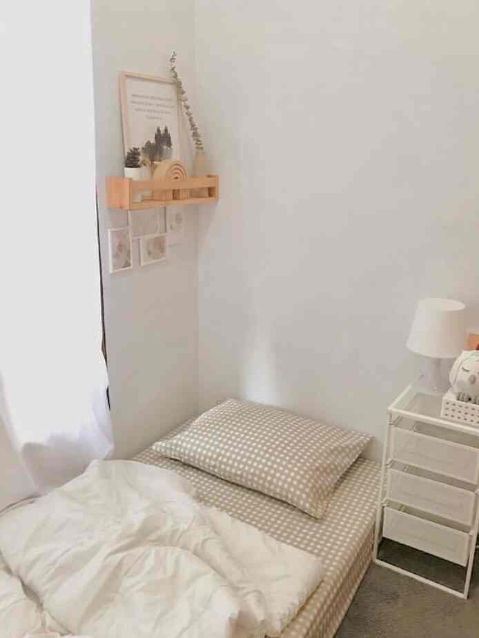 White and beige toned kids' room featuring a bed with pillow and bedding, beside a small drawer unit creating a cozy atmosphere