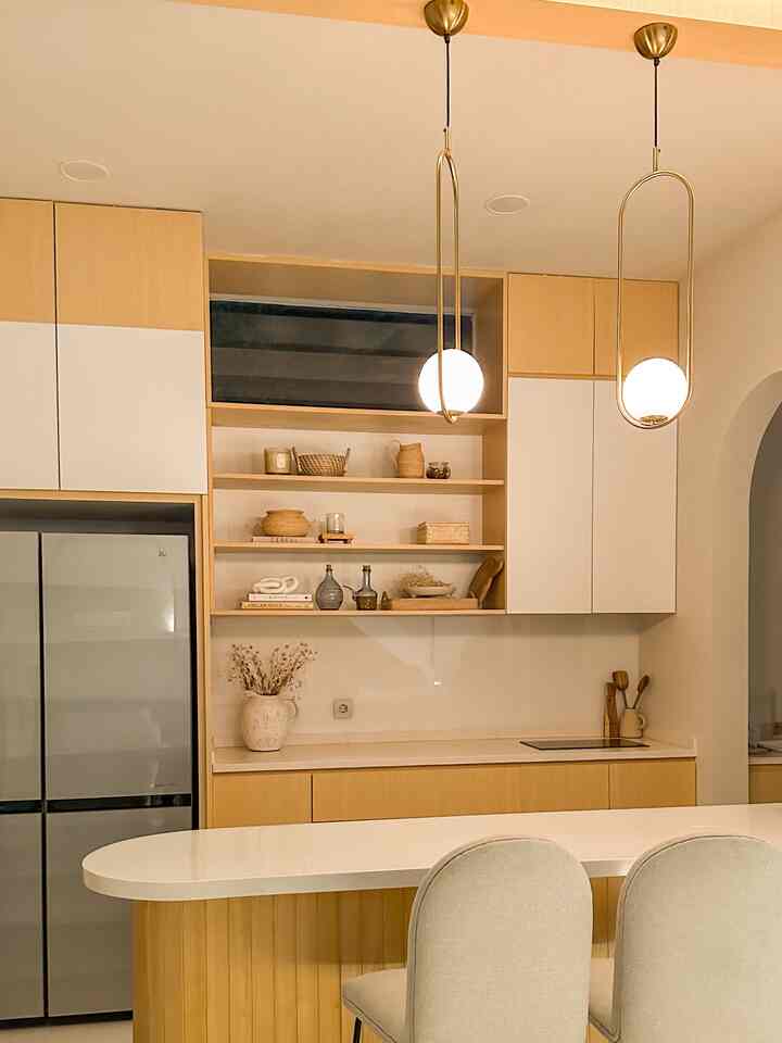 A modern kitchen space featuring soft gold and natural wood tones, with a white dining island and pendant lights creating a harmonious atmosphere