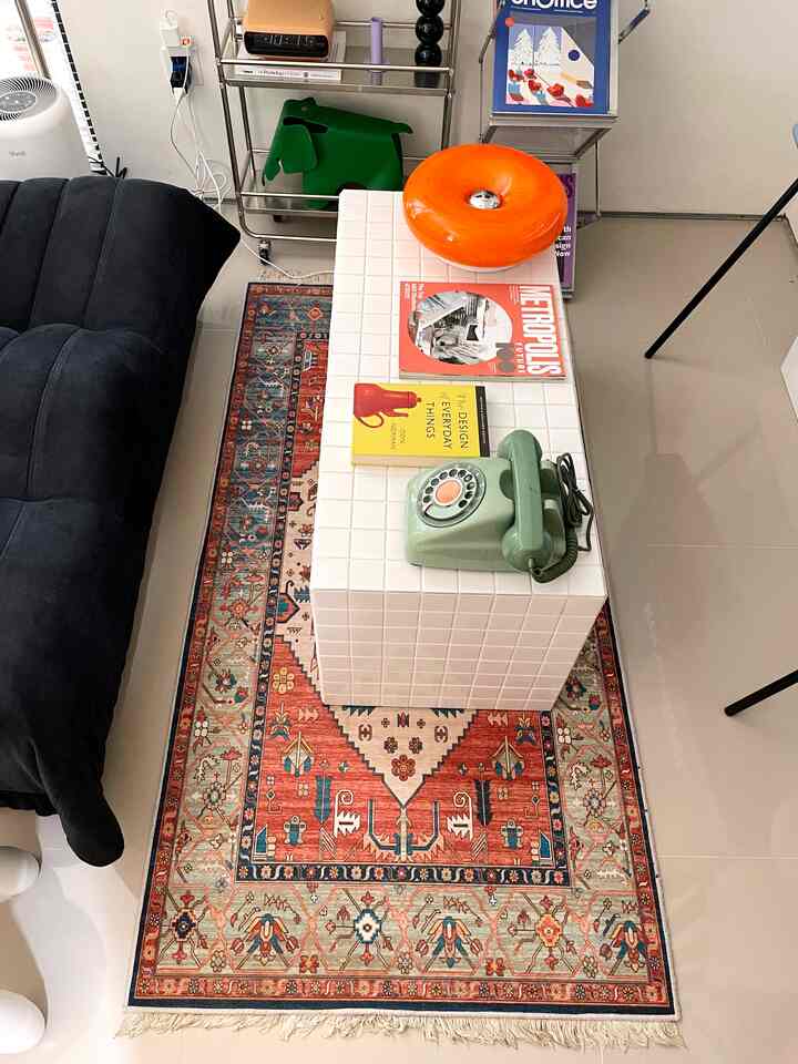 A living room with a white coffee table and black sofa, featuring vintage objects and a colorful patterned rug creating a cozy atmosphere