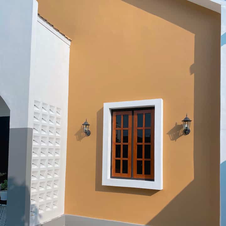 Beige wall facade with white-framed window and symmetrical wall sconces, showcasing a simple Scandinavian-style home exterior in morning light