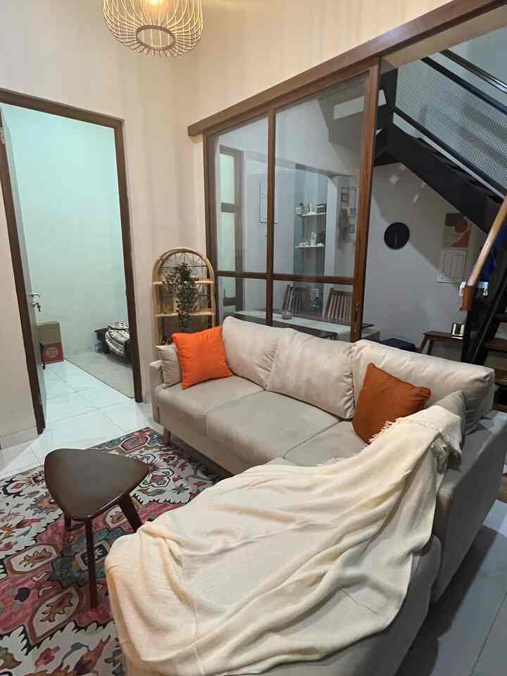 A beige living room with orange accent pillows, featuring a central sofa and small table creating a cozy atmosphere