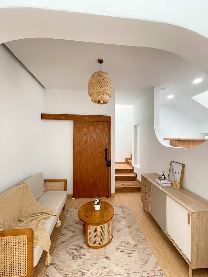 Small living room featuring natural wood tones and white walls, with a round rattan coffee table and two-seat sofa, simple and airy atmosphere