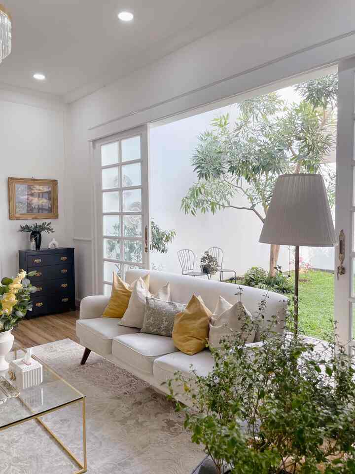 White and gold toned living room featuring a comfortable sofa, large window opening to garden, natural light and wood tone flooring accents
