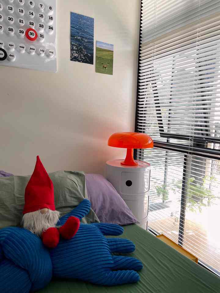 Clean bedroom with white walls and nightstand, green bedspread, and a red hat decoration as vibrant accents