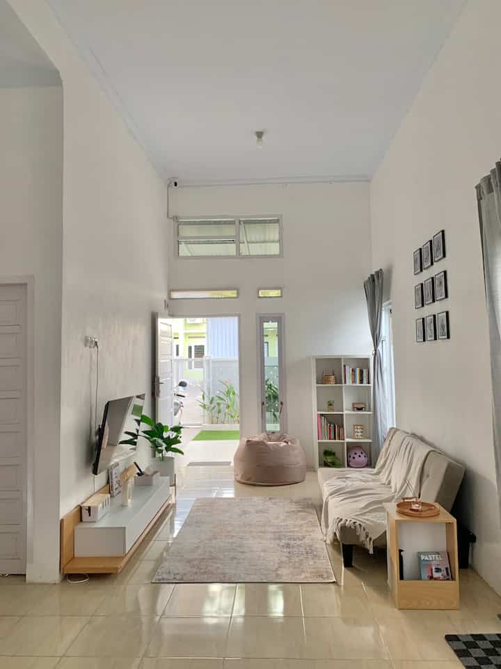 White and wood tone studio apartment living room featuring beige sofa, bean bag, bookshelf in a simple minimalist setting