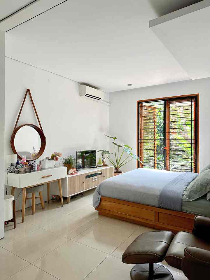 Simple and natural bedroom with white walls, wood tone bed, TV stand, and plants by balcony window