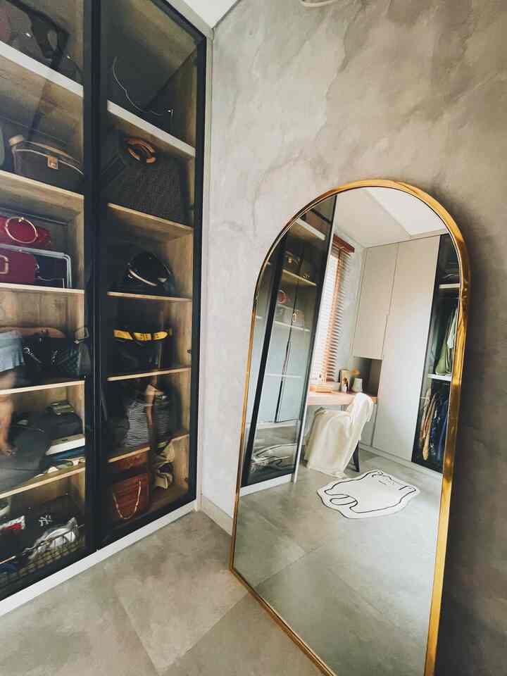 Gray industrial wall and gold-framed full-length mirror in a mini walk-in closet with a cat-shaped white carpet placed centrally