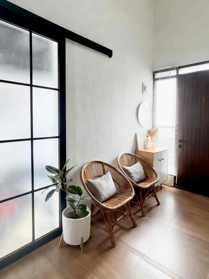 Natural wood tones and white backdrop entrance featuring rattan chairs and large potted plant creating a cozy atmosphere
