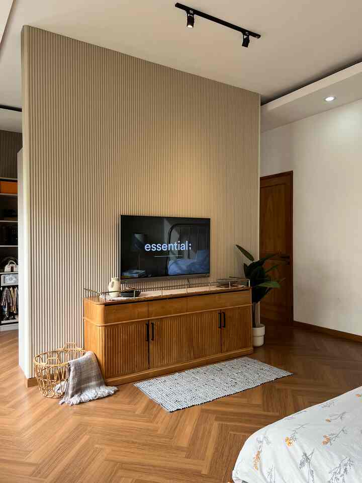 Natural color and wood tone bedroom featuring beige wall panel, herringbone flooring, TV and wooden cabinet creating a cozy space