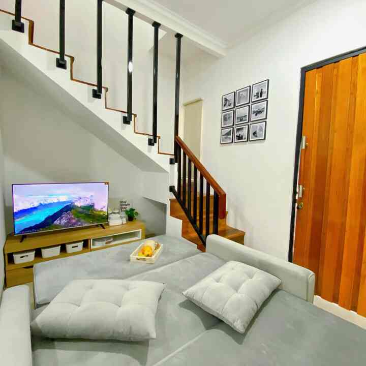 Natural tone living room featuring a gray sofa bed, wooden door, TV stand with compact and efficient layout under staircase