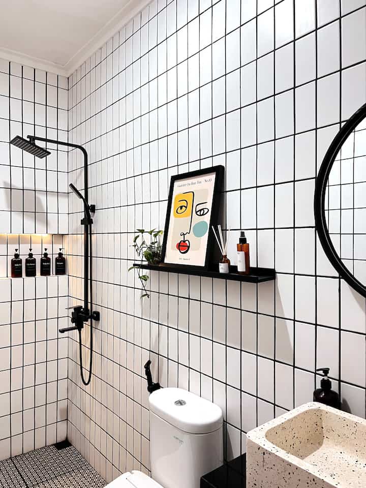 Bathroom with white tiled walls and black accents, featuring shower fixtures, sink, and framed wall art in a clean modern setting