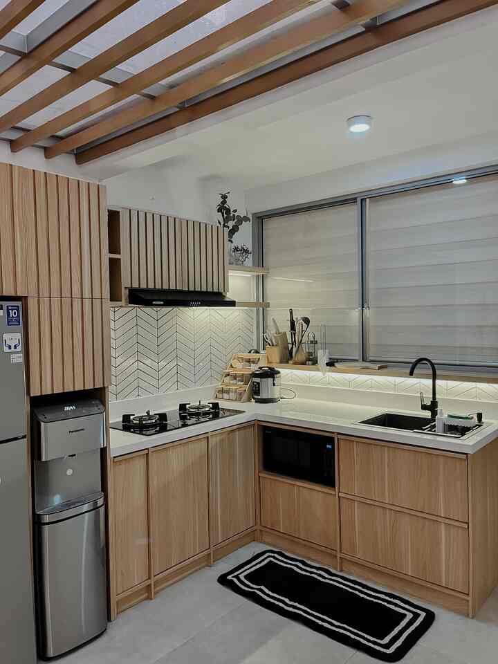 Modern L-shaped kitchen featuring white countertops and wood-toned cabinetry, with blinds on the window and contemporary kitchen appliances in a clean setting