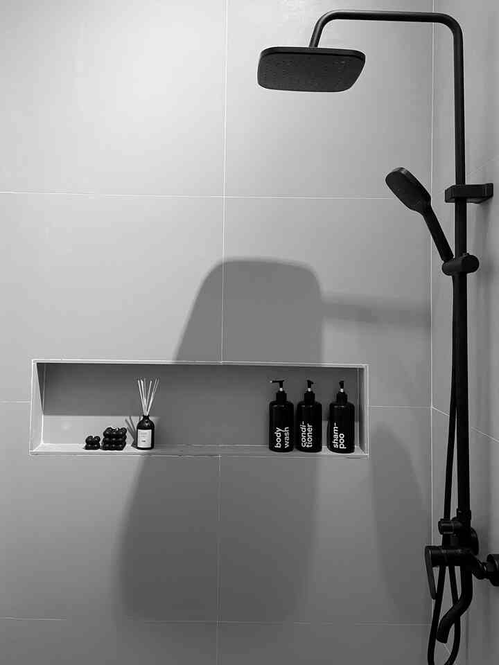 Monotone black and white bathroom featuring simple black shower fixtures and built-in niche with diffuser, creating a clean atmosphere