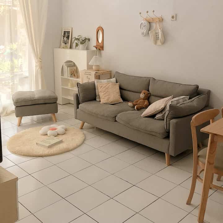 Natural-colored compact living room featuring a gray sofa, matching stool, and a round cream carpet creating a cozy atmosphere